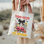Person holding a tote bag with Halloween-themed design featuring skulls, flowers, and text.